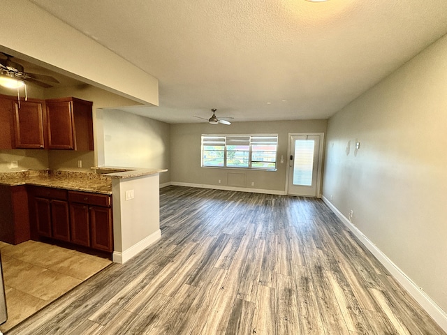 kitchen with open floor plan, light wood-style flooring, baseboards, a ceiling fan, and a peninsula