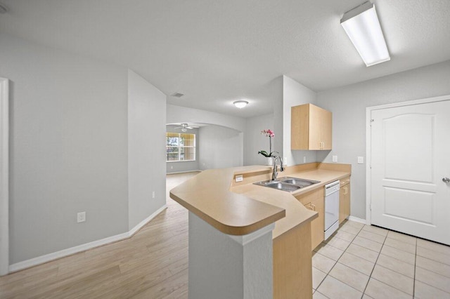 kitchen with a sink, light brown cabinets, dishwasher, a peninsula, and baseboards