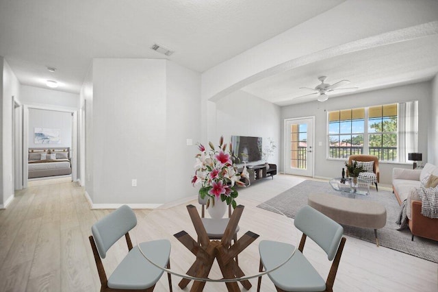living room featuring a ceiling fan, visible vents, arched walkways, baseboards, and light wood finished floors