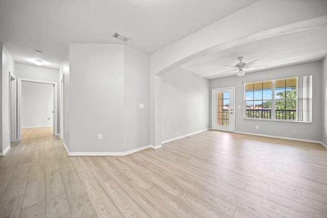 empty room featuring arched walkways, light wood-style flooring, a ceiling fan, baseboards, and visible vents