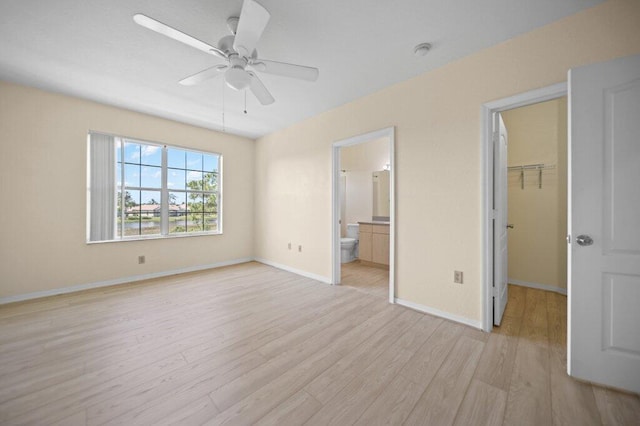 unfurnished bedroom with baseboards, a closet, light wood finished floors, connected bathroom, and a spacious closet