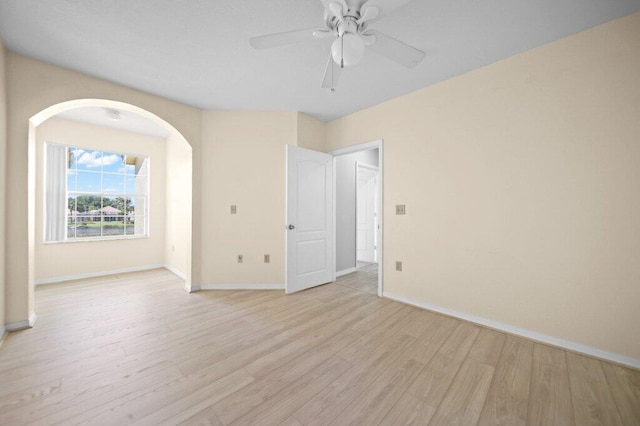 empty room with baseboards, a ceiling fan, light wood finished floors, and arched walkways