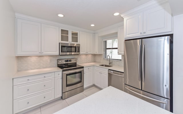 kitchen with appliances with stainless steel finishes, a sink, white cabinetry, light tile patterned floors, and backsplash
