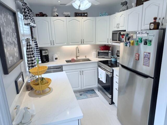 kitchen featuring light countertops, ceiling fan, appliances with stainless steel finishes, white cabinetry, and a sink