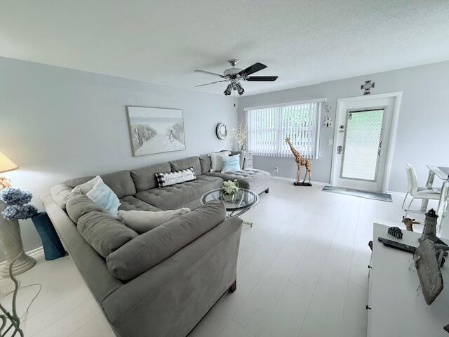 living room featuring a textured ceiling, wood finished floors, baseboards, and a ceiling fan