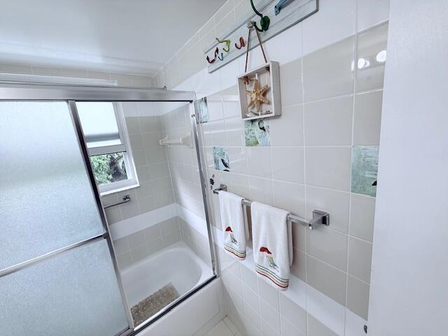 full bathroom featuring combined bath / shower with glass door and tile walls