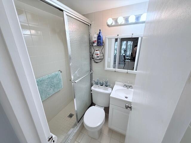 bathroom featuring toilet, vanity, tile walls, and a shower stall
