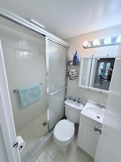 full bathroom with a shower stall, toilet, vanity, and tile walls