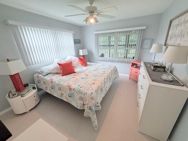 bedroom with baseboards, light wood-style flooring, ceiling fan, and a textured ceiling