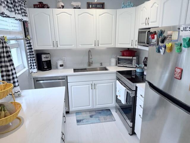 kitchen featuring light countertops, a sink, white cabinetry, appliances with stainless steel finishes, and a toaster