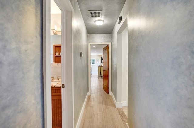 corridor with light wood finished floors, visible vents, and baseboards