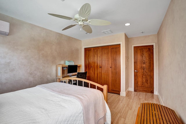 bedroom featuring light wood-style flooring, a closet, a ceiling fan, visible vents, and a wall mounted air conditioner