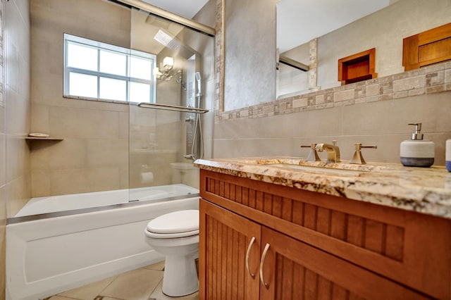 bathroom with combined bath / shower with glass door, vanity, tile patterned floors, toilet, and tile walls