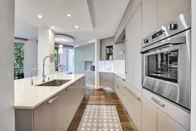 kitchen featuring decorative backsplash, dark wood-style flooring, oven, modern cabinets, and a sink