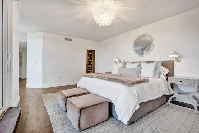 bedroom with a notable chandelier, a textured ceiling, wood-type flooring, baseboards, and visible vents