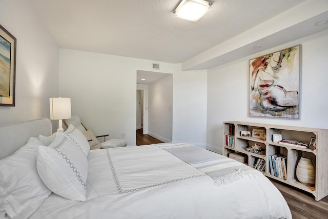 bedroom featuring baseboards, visible vents, a textured ceiling, and wood finished floors