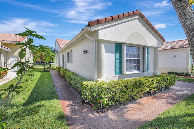 view of property exterior featuring stucco siding, a tiled roof, and a yard