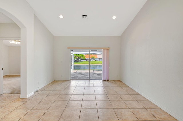 empty room featuring light tile patterned flooring, baseboards, visible vents, and vaulted ceiling