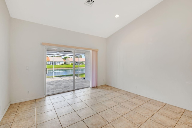 empty room featuring vaulted ceiling, recessed lighting, light tile patterned floors, a water view, and visible vents