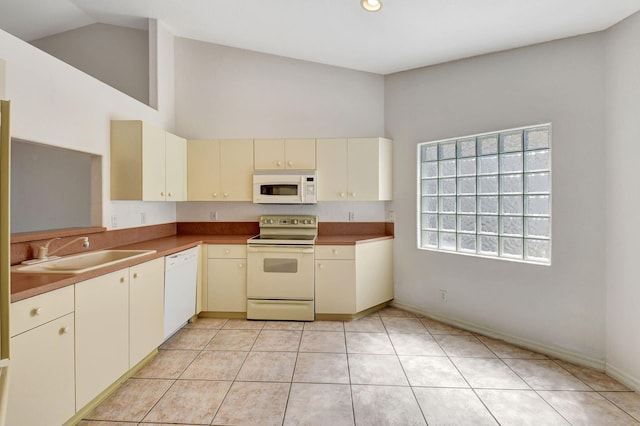 kitchen featuring high vaulted ceiling, cream cabinetry, white appliances, a sink, and light tile patterned floors
