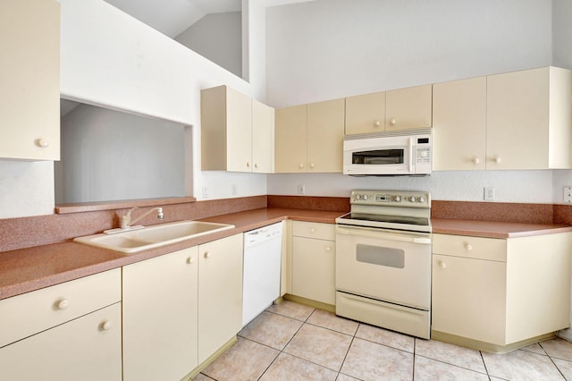 kitchen with high vaulted ceiling, cream cabinetry, white appliances, a sink, and light tile patterned floors