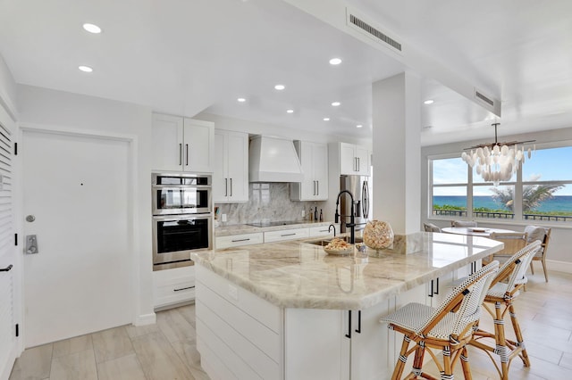 1149 Hillsboro Mile Unit 112N, Hillsboro Beach, FL 33062 - kitchen featuring backsplash, appliances with stainless steel finishes, premium range hood, a kitchen island with sink, and visible vents