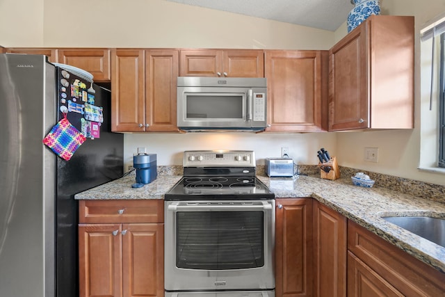 301 Norwood Ter Unit N230, Boca Raton, FL 33431 - kitchen with brown cabinetry, stainless steel appliances, light stone counters, and vaulted ceiling
