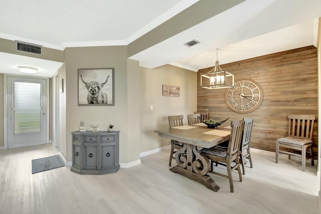 dining area with a chandelier, wood walls, visible vents, and light wood finished floors