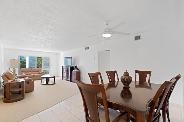 dining space with a textured ceiling, light tile patterned floors, light colored carpet, visible vents, and ceiling fan