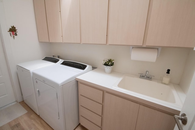 washroom featuring light wood-style flooring, washing machine and clothes dryer, cabinet space, and a sink