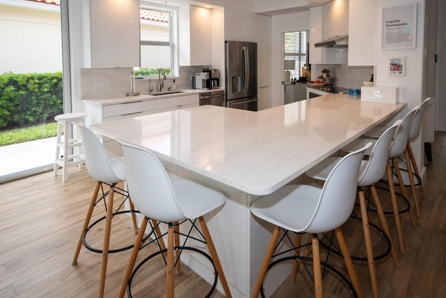 kitchen with a sink, a kitchen bar, under cabinet range hood, stainless steel appliances, and light wood-style floors