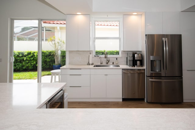 kitchen with light countertops, tasteful backsplash, a sink, beverage cooler, and appliances with stainless steel finishes