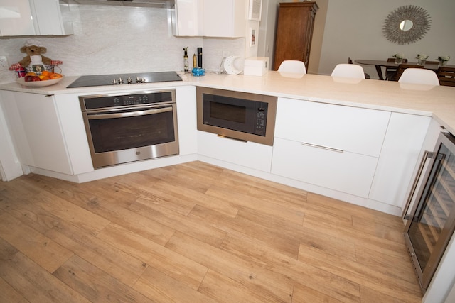 kitchen with black electric cooktop, oven, light wood-style floors, built in microwave, and white cabinets