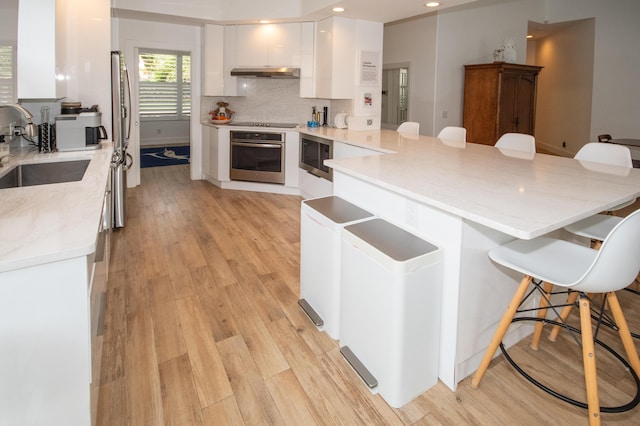 kitchen with a kitchen bar, under cabinet range hood, a sink, and stainless steel appliances