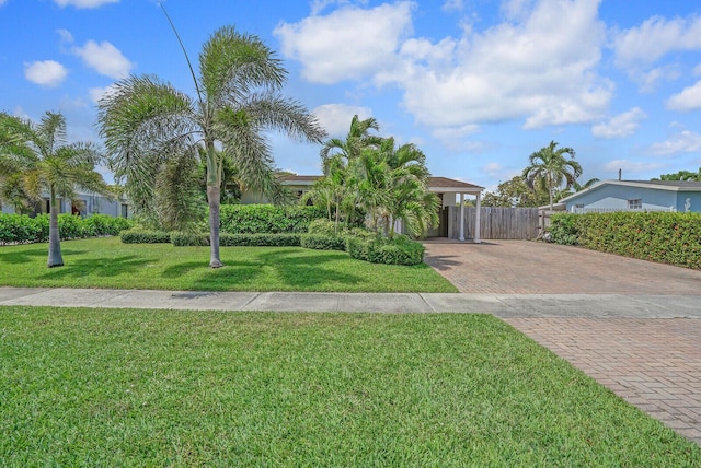 view of property hidden behind natural elements featuring a front lawn, decorative driveway, and fence