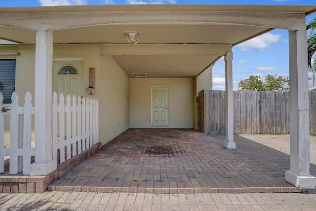 doorway to property with stucco siding, fence, a carport, and visible vents