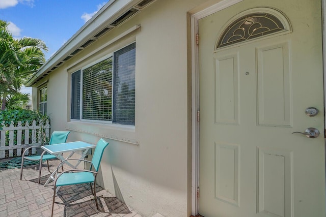 view of exterior entry with stucco siding, fence, and a patio area