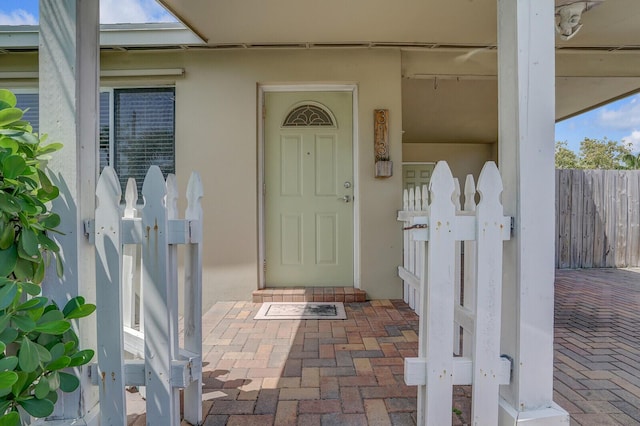 entrance to property featuring stucco siding and fence