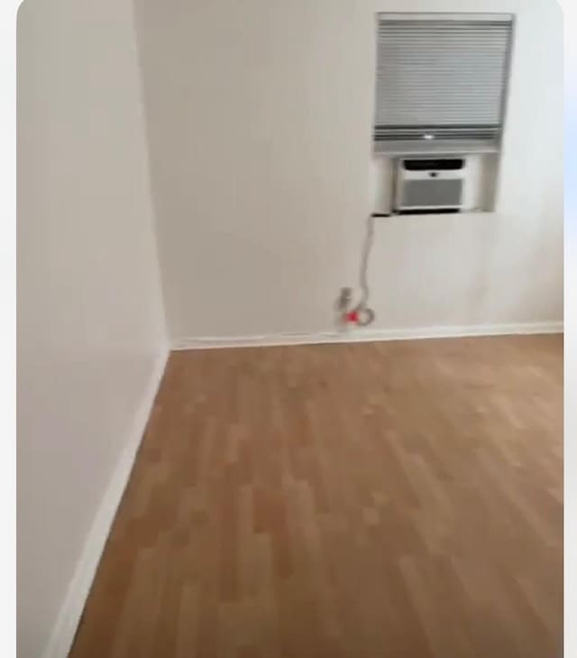 unfurnished room with cooling unit, baseboards, and wood finished floors