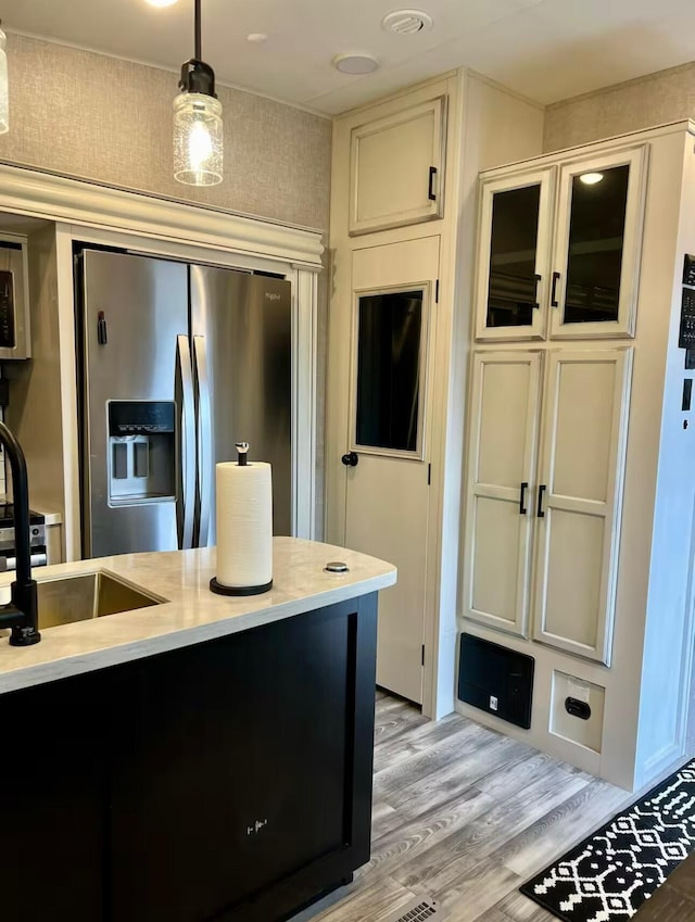 kitchen featuring light countertops, a sink, light wood finished floors, stainless steel fridge with ice dispenser, and hanging light fixtures