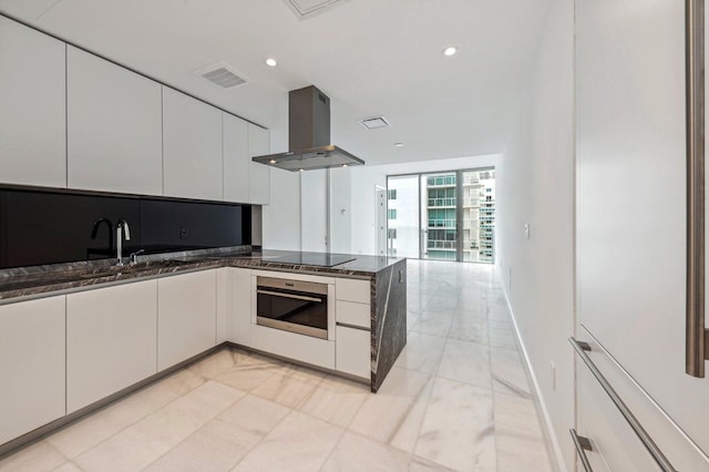 kitchen featuring black electric cooktop, stainless steel oven, island range hood, white cabinets, and a peninsula