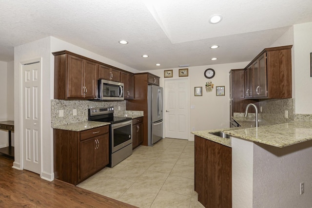 kitchen with a sink, appliances with stainless steel finishes, light stone counters, and a peninsula
