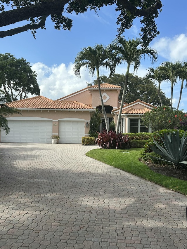 mediterranean / spanish-style home with a front yard, decorative driveway, stucco siding, an attached garage, and a tile roof