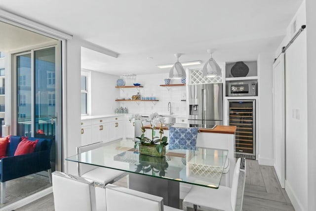 dining area featuring a barn door, bar, beverage cooler, light wood-style flooring, and baseboards