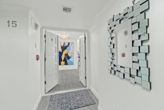 hallway with crown molding, baseboards, wood finished floors, and visible vents