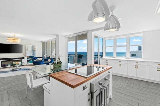 kitchen featuring butcher block counters, open floor plan, black electric cooktop, a water view, and white cabinetry