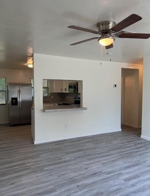 unfurnished living room featuring baseboards, wood finished floors, and a ceiling fan