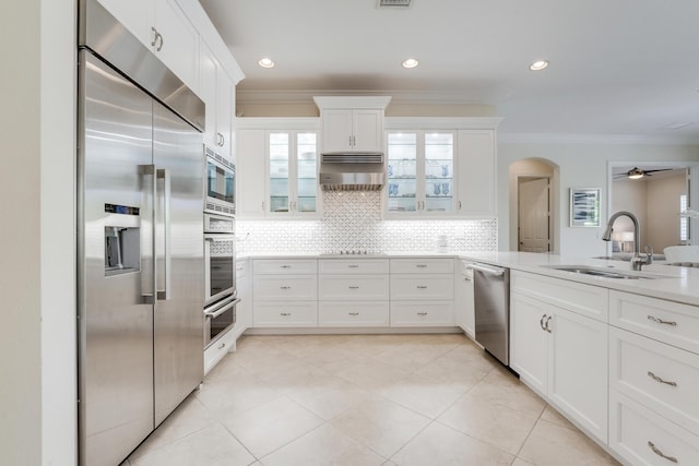 12479 Aviles Cir, Palm Beach Gardens, FL 33418 - kitchen featuring built in appliances, a sink, crown molding, decorative backsplash, and arched walkways
