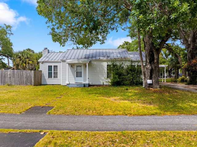 view of front of home featuring a front yard, a standing seam roof, a chimney, fence, and metal roof