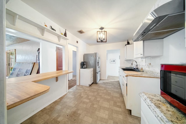 kitchen with light countertops, a sink, stainless steel fridge with ice dispenser, wall chimney exhaust hood, and visible vents